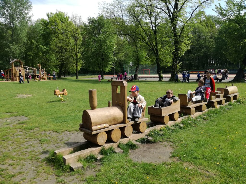 Przedszkolaki podczas zabawy na placu zabaw. Siedzą w wagonikach drewnianej kolejki