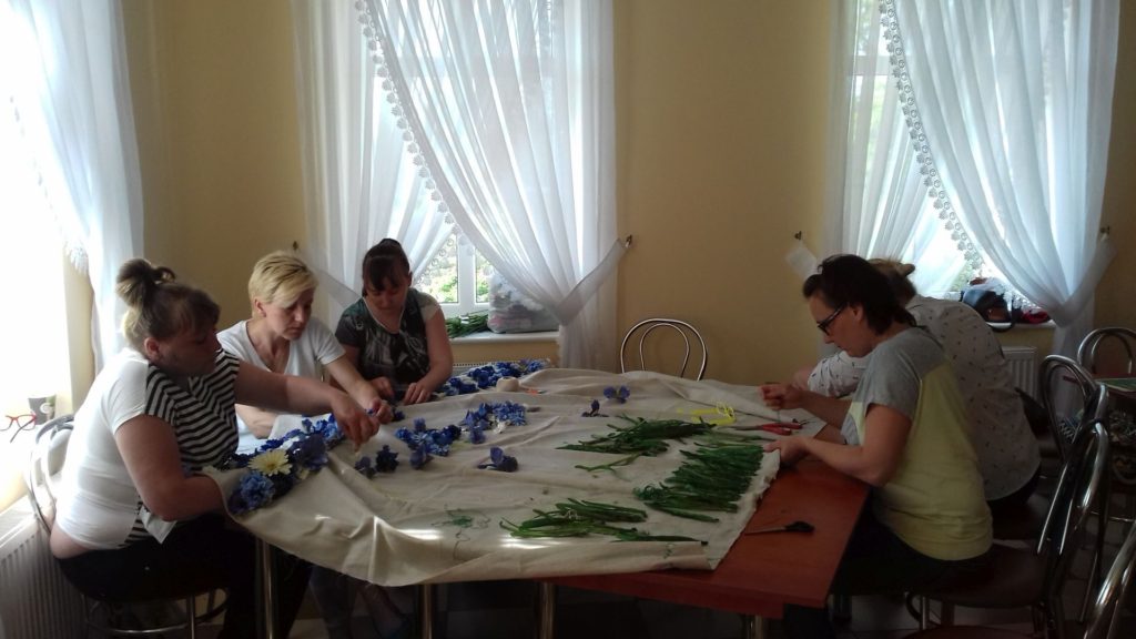 Podczas spotkania w klubie samopomocy w Dębnie uczestniczki przy stole przygotowują obraz z kwiatów