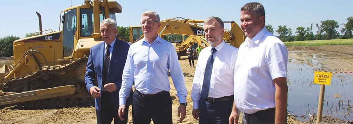 Na zdjęciu: Czterech przedstawicieli gmin stoi na placu budowy zbiornika. W tle widać żółtą koparkę.