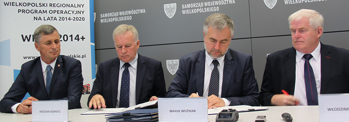 Na zdjęciu czterech mężczyzn w garniturach podpisuje dokumenty. Fotografia pochodzi z archiwum Urzędu Marszałkowskiego Województwa Wielkopolskiego.