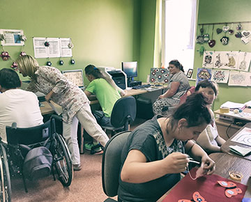Na zdjęciu uczestnicy projektu w sali pracują przy komputerach. Jedna osoba porusza się na wózku inwalidzkim. Zdjęcie pochodzi z archiwum beneficjenta.