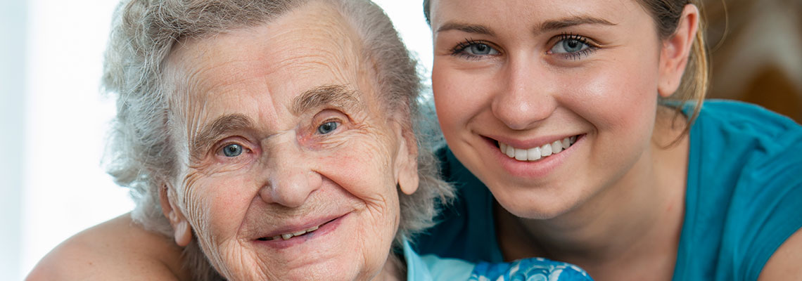 Fotografia przedstawia młodą kobietę przytulającą uśmiechniętą staruszkę. Zdjęcie pochodzi z Obrazy licencjonowane przez Depositphotos.com/Drukarnia Chroma.