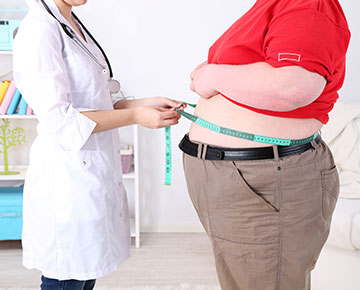 Fotografia przedstawia otyłego mężczyznę, który stoi na wadze. Zdjęcie pochodzi z Obrazy licencjonowane przez Depositphotos.com/Drukarnia Chroma.