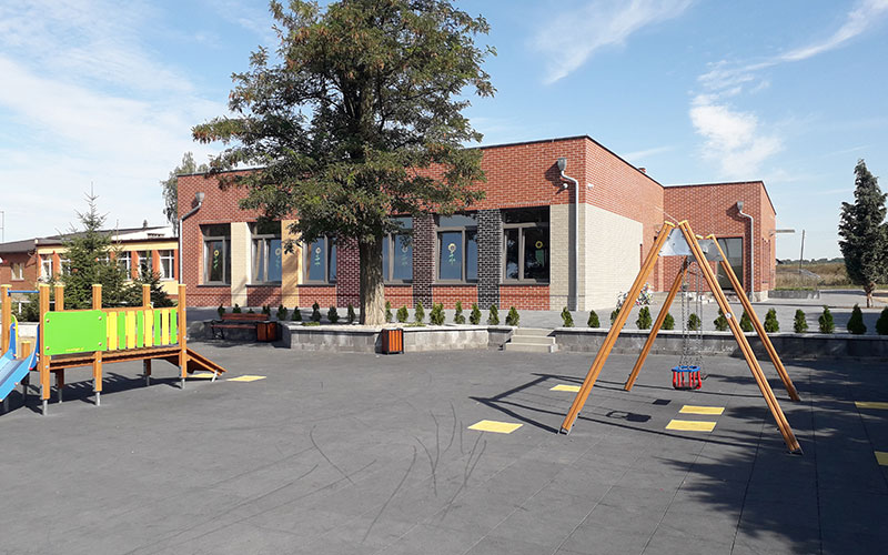 Fotografia przedstawia plac zabaw na tle nowoczesnego budynku szkoły. Zdjęcie pochodzi z archiwum beneficjenta.