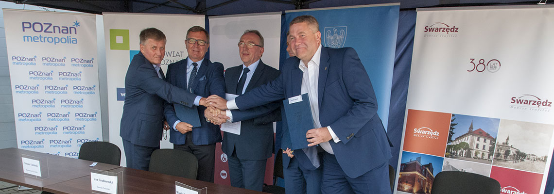Fotografia przedstawia oficjeli podpisujących umowę, którzy wymieniają uściski dłoni. Autorem zdjęcia jest Jarosław Tomaszewski.