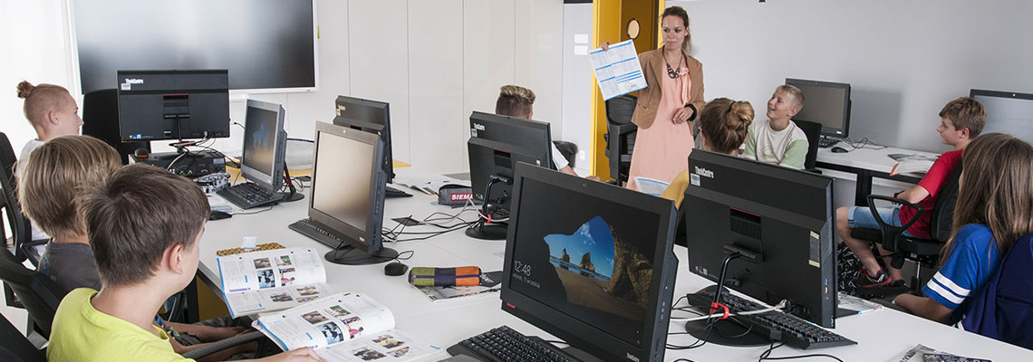 Fotografia przedstawia dzieci uczące się w nowocześnie wyposażonej pracowni komputerowej. Autorem zdjęcia jest Jarosław Tomaszewski.