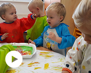 Fotografia przedstawia małe dzieci w kolorowych fartuchach, bawiące się farbami. Zdjęcie pochodzi z archiwum beneficjenta.