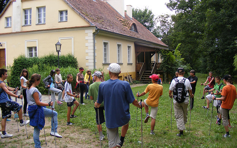 Fotografia przedstawia grupę osób, która rozgrzewa się przed wyruszeniem w trasę. Zdjęcie pochodzi z archiwum Zespołu Parków Krajobrazowych Województwa Wielkopolskiego.