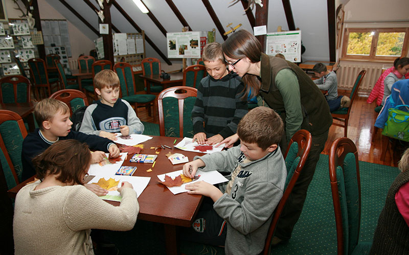  Fotografia przedstawia dzieci przy stolikach, które wykonują prace plastyczne z wykorzystaniem liści. Zdjęcie pochodzi z archiwum Nadleśnictwa Oborniki.