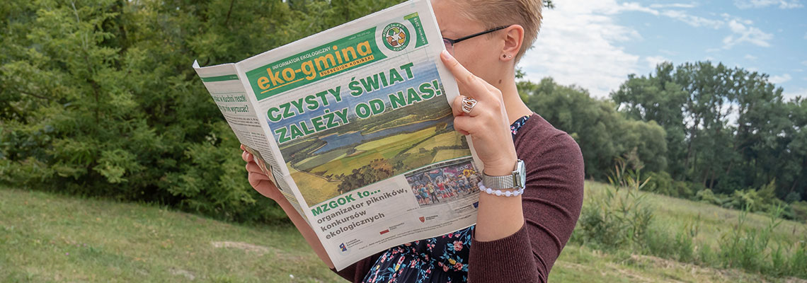 Fotografia przedstawia kobietę czytającą informator „Eko-Gmina”. Autorem zdjęcia jest Maciej Motylewski.
