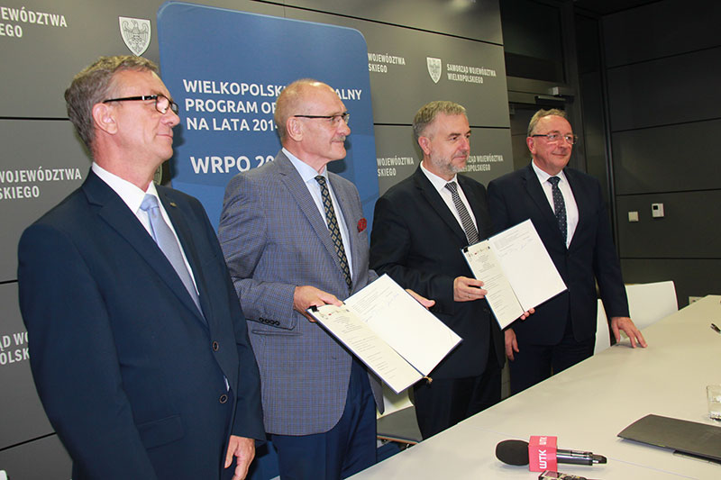 Fotografia przedstawia czterech mężczyzn w garniturach, prezentujących podpisaną chwilę wcześniej umowę. Zdjęcie pochodzi z archiwum Urzędu Marszałkowskiego Województwa Wielkopolskiego.