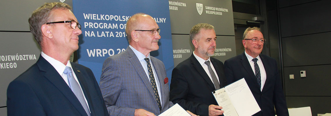 Fotografia przedstawia czterech mężczyzn w garniturach, prezentujących podpisaną chwilę wcześniej umowę. Zdjęcie pochodzi z archiwum Urzędu Marszałkowskiego Województwa Wielkopolskiego.