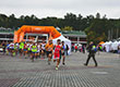 Fotografia przedstawia kilkudziesięciu biegaczy w kolorowych strojach, którzy rozpoczęli wyścig z miejsca startowego. Autorem zdjęcia jest firma Sun and More.