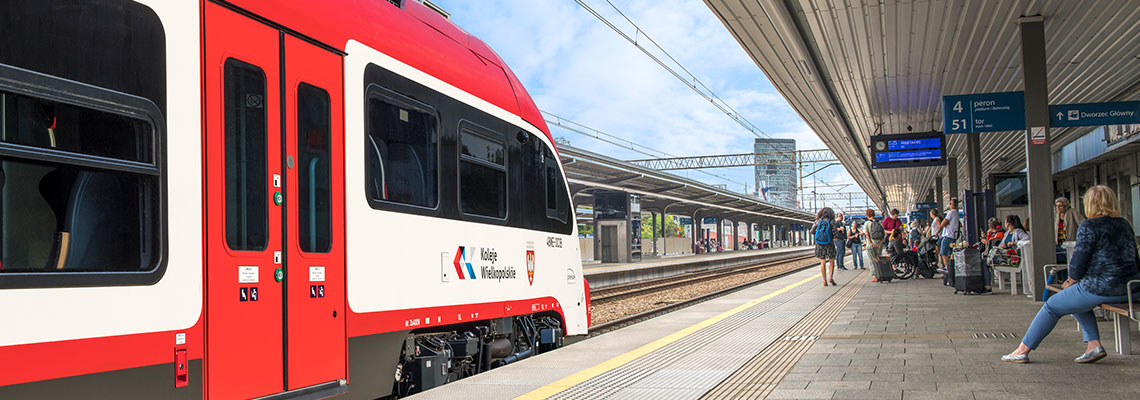 Fotografia przedstawia pociąg Elf 2 w czerwono-białych barwach, z napisem „Koleje Wielkopolskie”, który stoi przy peronie na dworcu Poznań Główny oraz ludzi czekających na peronie. Zdjęcie pochodzi z archiwum beneficjenta.