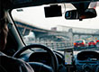 Fotografia przedstawia wnętrze samochodu ukazane spomiędzy fotela kierowcy i pasażera. Za kierownicą siedzi mężczyzna. Za szybą widać rozmyty obraz drogowego korka. Zdjęcie pochodzi z archiwum beneficjenta.
