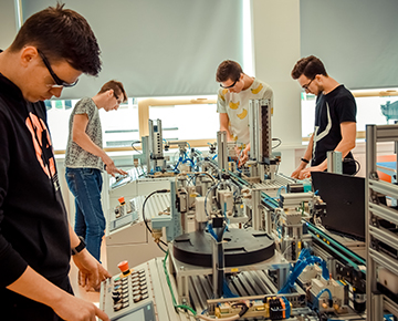 Fotografia przedstawia piątkę młodych uczniów pracujących na nowoczesnym sprzęcie w pracowni automatyki przemysłowej. Zdjęcie pochodzi z archiwum beneficjenta.