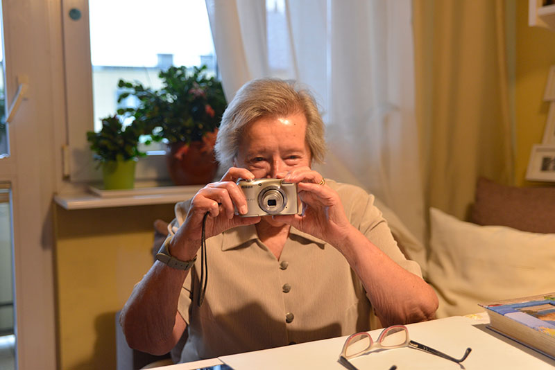 Fotografia przedstawia panią Ewę, która robi fotografowi zdjęcie aparatem cyfrowym. Autorem zdjęcia jest Dominik Wójcik.