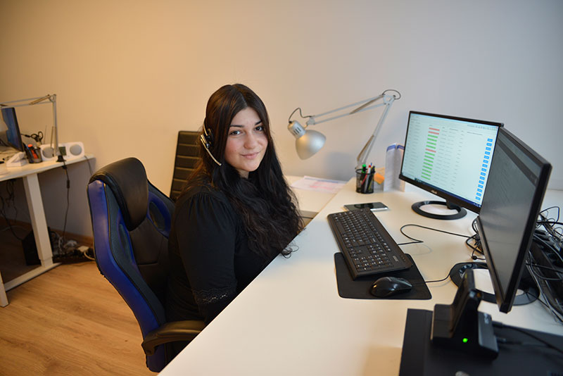 Fotografia przedstawia Patrycję Basińską – teleasystentkę, siedząca na stanowisku pracy – przy komputerze z dwoma monitorami, ze słuchawką na głowie. Autorem zdjęcia jest Dominik Wójcik.