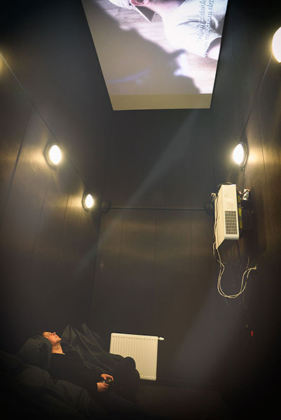 Fotografia przedstawia mężczyznę korzystającego z sali kinowej Mediateki. Mężczyzna leży w wygodnych fotelach, a film wyświetlany jest na suficie pomieszczenia. Autorem zdjęcia jest Łukasz Karkoszka.
