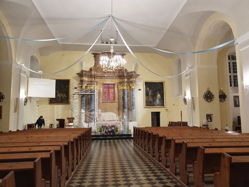 Fotografia przedstawia nawę główną niewielkiego kościoła. Po obu stronach widać drewniane ławki, na wprost – prezbiterium, które jest w remoncie. Widać rusztowanie. Zdjęcie pochodzi z archiwum beneficjenta.