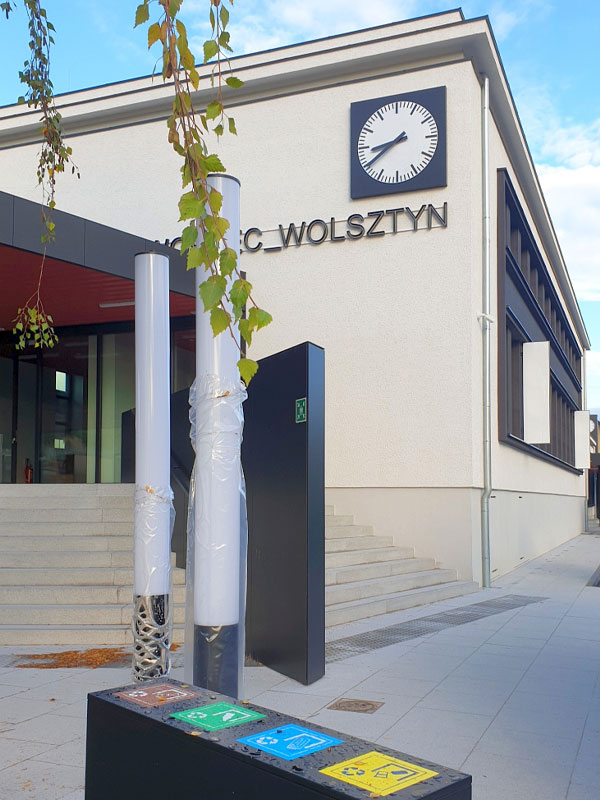 Fotografia przedstawia widok z zewnątrz na główne wejście do dworca kolejowego w Wolsztynie. Poza przeszklonymi drzwiami, na elewacji widać zegar oraz napis Dworzec Wolsztyn. Zdjęcie pochodzi z archiwum Urzędu Miejskiego w Wolsztynie.
