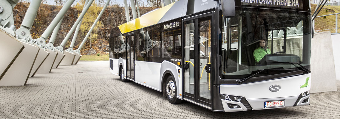Fotografia przedstawia nowoczesny autobus Urbino LE Lite, firmy Solaris. Pojazd ma dwoje drzwi, jest wykonany w białych, czarnych i żółtych barwach. Za kierownicą siedzi kobieta, na wyświetlaczu jest napis „Światowa premiera”. Zdjęcie pochodzi z archiwum beneficjenta.
