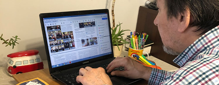 Fotografia przedstawia Krzysztofa Tomkiela – mężczyznę w koszuli w kratę, który siedzi przy stoliku i pracuje przy komputerze. Obok leży kilka gazet. Zdjęcie pochodzi z archiwum prywatnego.