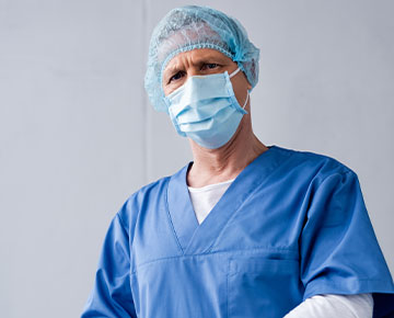 Fotografia przedstawia lekarza ubranego w niebieski fartuch i czepek oraz białe rękawiczki. Zdjęcie pochodzi z Obrazy licencjonowane przez Depositphotos.com/Drukarnia Chroma.