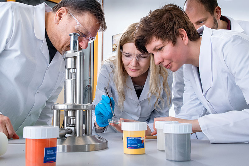 Fotografia przedstawia cztery osoby – dwie kobiety i dwóch mężczyzn, w laboratoryjnych fartuchach, które wspólnie badają próbkę. Dwie z osób mają ochronne okulary. Zdjęcie pochodzi z archiwum beneficjenta.
