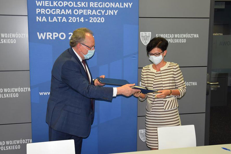 Fotografia przedstawia mężczyznę w garniturze oraz elegancko ubraną kobietę, którzy przekazują sobie podpisane umowy. Zdjęcie pochodzi z archiwum Urzędu Marszałkowskiego Województwa Wielkopolskiego.