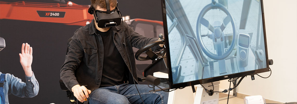 Fotografia przedstawia mężczyznę siedzącego za kierownicą symulatora. Na oczach ma gogle VR. Na przeciw niego znajduje się stanowisko komputerowe, prawdopodobnie instruktora. Zdjęcie pochodzi z archiwum beneficjenta.