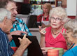 Fotografia przedstawia czterech seniorów – dwie kobiety i dwóch mężczyzn, którzy rozmawiają przy stole. Na blacie stoi otwarty laptop. Zdjęcie pochodzi z Obrazy licencjonowane przez Depositphotos.com/Drukarnia Chroma.
