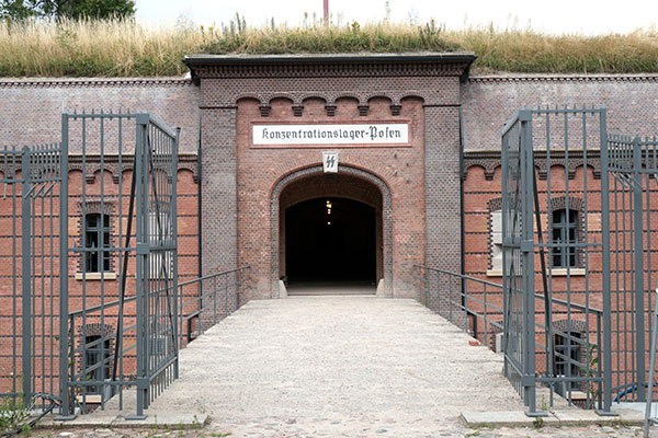 Fotografia przedstawia bramę do Fortu VII. Na pomoście widoczna jest brama kratowana, następna jest już murowana. Nad nią widnieje napis Konzentrationlager Posen, czyli obóz koncentracyjny Poznań. Zdjęcie pochodzi z archiwum beneficjenta.