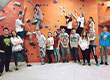 Fotografia przedstawia kilkunastoosobową grupę młodzieży, która pozuje na tle ścianki wspinaczkowej. Większość osób stoi, pięć osób pozuje na samej ściance. Zdjęcie pochodzi z archiwum beneficjenta.