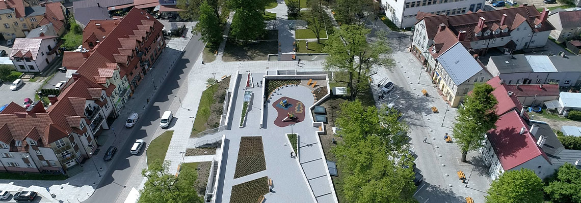 Fotografia z lotu ptaka przedstawia odnowione centrum miasta. Widać odnowiony plac, niewielki park z drzewami, a takżę ulice i zabudowania miejskie. Zdjęcie pochodzi z archiwum Urzędu Marszałkowskiego Wójewództwa Wielkopolskiego.