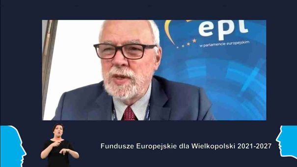 Fotografia jest zrzutem ekranu z wideokonferencji. W kadrze widoczny jest Jan Olbrycht, poseł do Parlamentu Europejskiego. W lewym dolnym rogu ekranu jest kobieta, która tłumaczy wypowiedź na język migowy. Zdjęcie pochodzi z archiwum Urzędu Marszałkowskiego Województwa Wielkopolskiego.