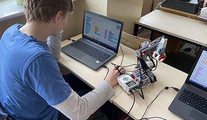 Fotografia przedstawia ucznia, który przy laptopie programuje niewielkiego robota. Zdjęcie pochodzi z archiwum beneficjenta.