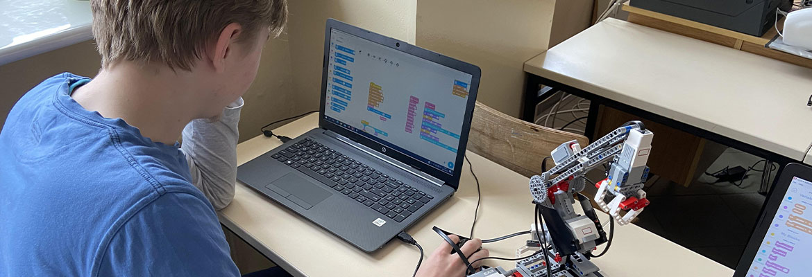 Fotografia przedstawia ucznia, który przy laptopie programuje niewielkiego robota. Zdjęcie pochodzi z archiwum beneficjenta.