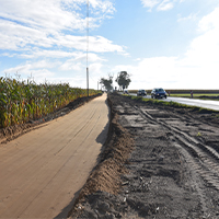Fotografia przedstawia rozkopany fragment drogi. Po prawej widać jadący samochód, z lewej pole kukurydzy. Zdjęcie pochodzi z archiwum WZDW.