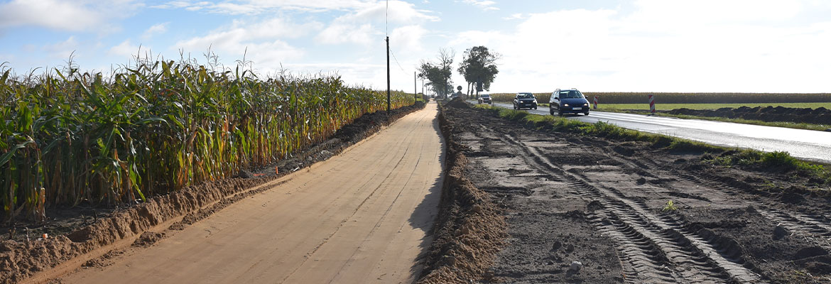 Fotografia przedstawia rozkopany fragment drogi. Po prawej widać jadący samochód, z lewej pole kukurydzy. Zdjęcie pochodzi z archiwum WZDW.