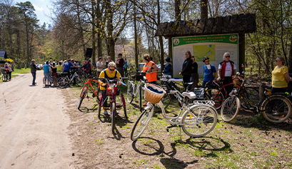 Fotografia przedstawia grupę kilkudziesięciu rowerzystów, czekających na skraju lasu. Zdjęcie pochodzi z archiwum beneficjenta.