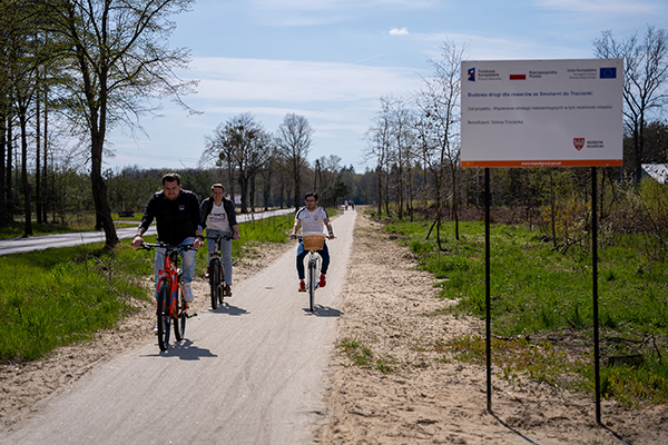 Fotografia przedstawia trzech rowerzystów jadących ścieżką rowerową. Po prawej stronie widać tablicę informacyjną o tym, że projekt był finansowany z budżetu Unii Europejskich. Zdjęcie pochodzi z archiwum beneficjenta.