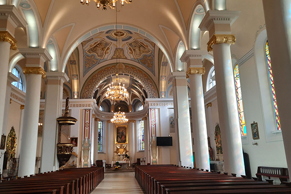 Fotografia przedstawia nawę główną kościoła. Widoczne są ławki, okrągłe filary, ołtarz i prezbiterium, a także freski na kolebkowym sklepieniu. Zdjęcie pochodzi z archiwum beneficjenta.