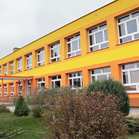 Fotografia przedstawia fasadę szkoły po termomodernizacji. Widoczna jest elewacja w pomarańczowo-czerwonych-żółych barwach. Zdjęcie pochodzi z archiwum beneficjenta.