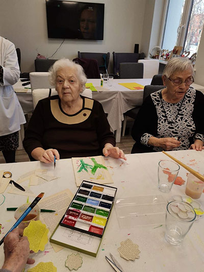 Fotografia przedstawia dwie starsze panie, które malują farbami przy stole. Zdjęcie pochodzi z archiwum beneficjenta.