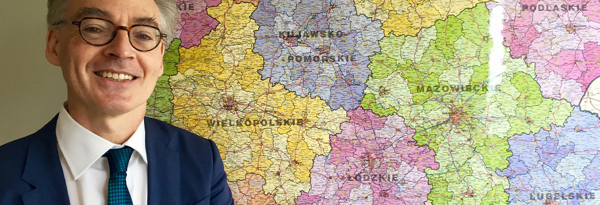 Fotografia przedstawia Christophera Todda, Dyrektora Wydziału ds. Polski w Dyrekcji Generalnej ds. Polityki Regionalnej i Miejskiej Komisji Europejskiej. To uśmiechnięty mężczyzna w garniturze i okularach. Pozuje na tle mapy polski, na której widoczne są województwa. Zdjęcie pochodzi z archiwum Komisji Europejskiej.
