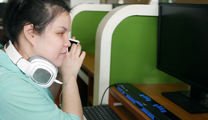 Fotografia przedstawia dziewczynę, prawdopodobnie niepełnosprawną, która siedzi przy biurku w pracy. Ma słuchawki, rozmawia przez telefon. Zdjęcie pochodzi z fot. Obrazy licencjonowane przez Depositphotos.com/Drukarnia Chroma.