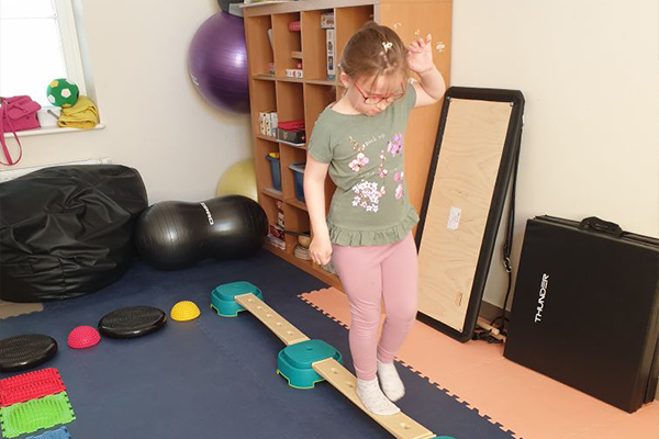 Fotografia przedstawia dziewczynkę ćwiczącą utrzymanie równowagi, chodząc po cienkiej platformie. Zdjęcie pochodzi z archiwum beneficjenta.