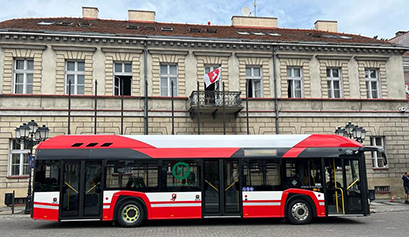 Fotografia przedstawia nowoczesny, biało-czerwony autobus komunikacji miejskiej, zaparkowany na tle budynku. Zdjęcie pochodzi z archiwum Miejskiego Zakładu Komunikacji.