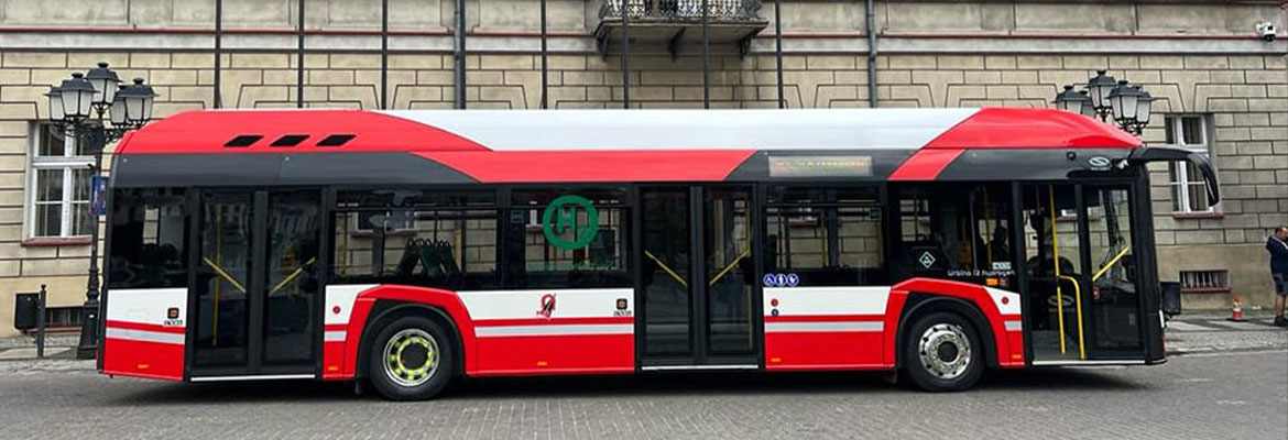 Fotografia przedstawia nowoczesny, biało-czerwony autobus komunikacji miejskiej, zaparkowany na tle budynku. Zdjęcie pochodzi z archiwum Miejskiego Zakładu Komunikacji.